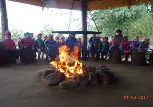 Dzieci siedzą w kole wokół ogniska.